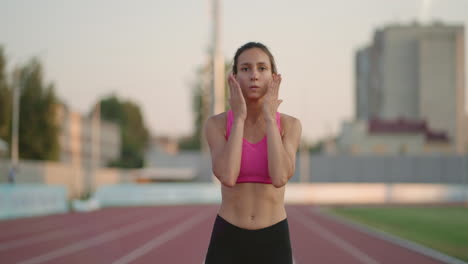 A-young-woman-athlete-brooding-warms-up-and-prepares-for-the-start-of-a-sprint-race-on-a-sunny-day-on-the-treadmill-of-the-stadium